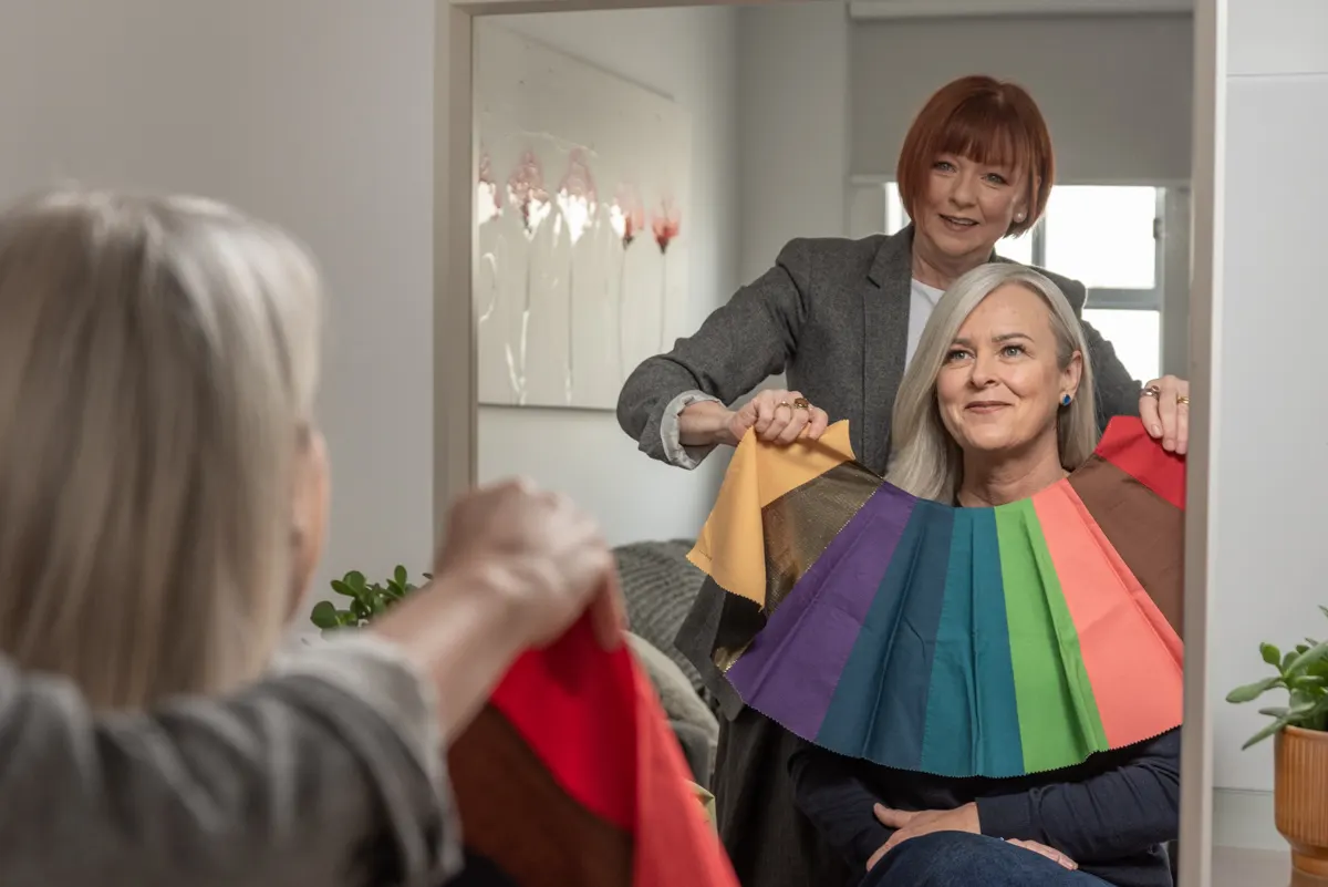 Steph holding colour swatches beneath a client's face in front of a mirror